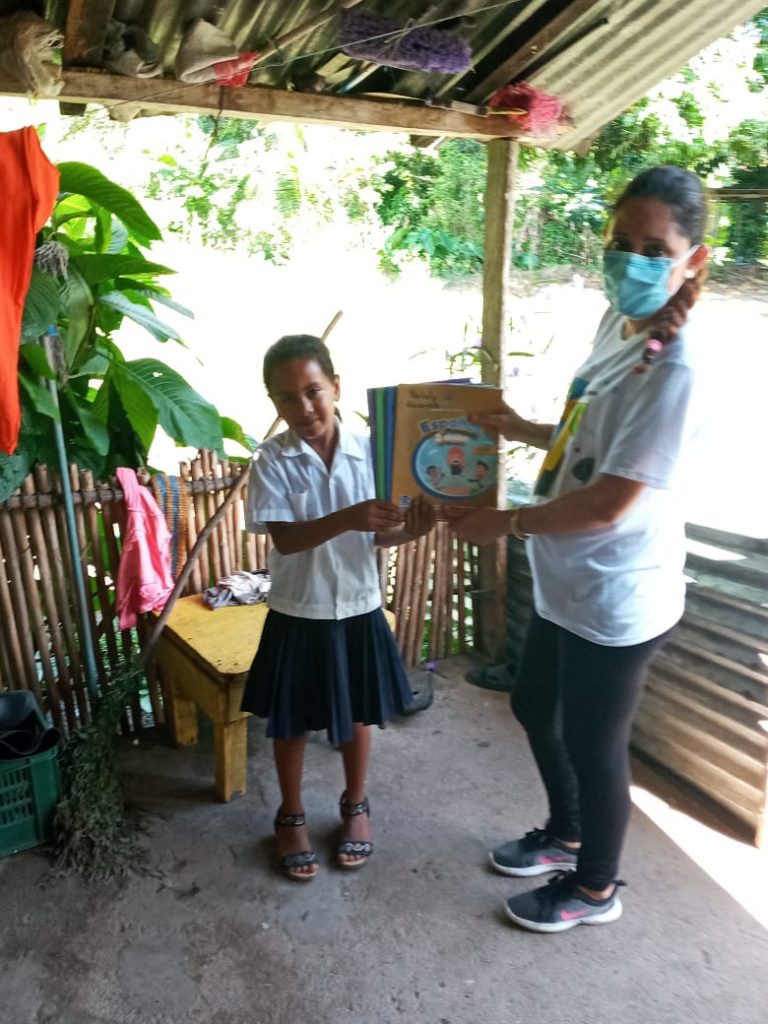 Maestra entrega material didáctico a una alumna.