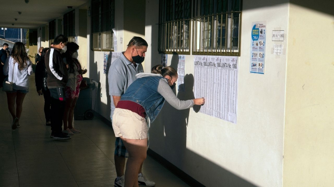 Personas mirando los listados antes de ejercer el sufragio en las elecciones en Costa Rica