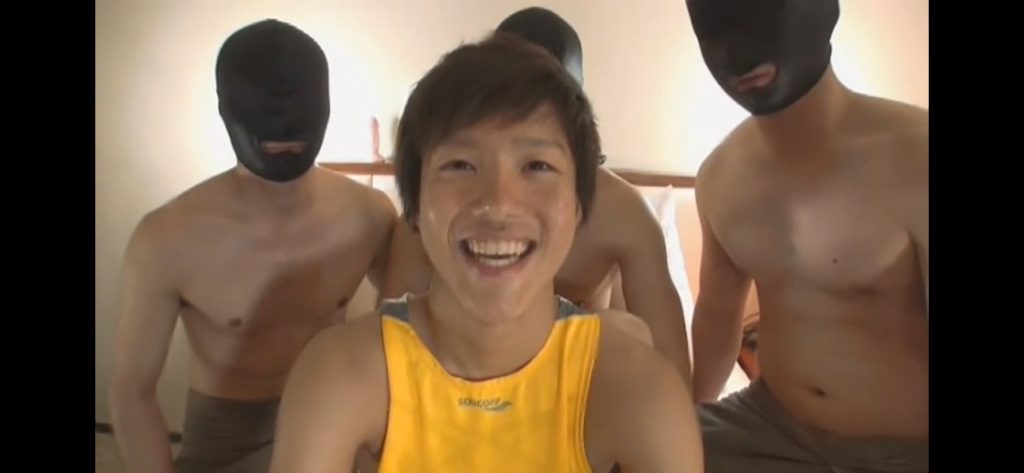 Kazuto sonriendo mientras atrás hay tres hombres